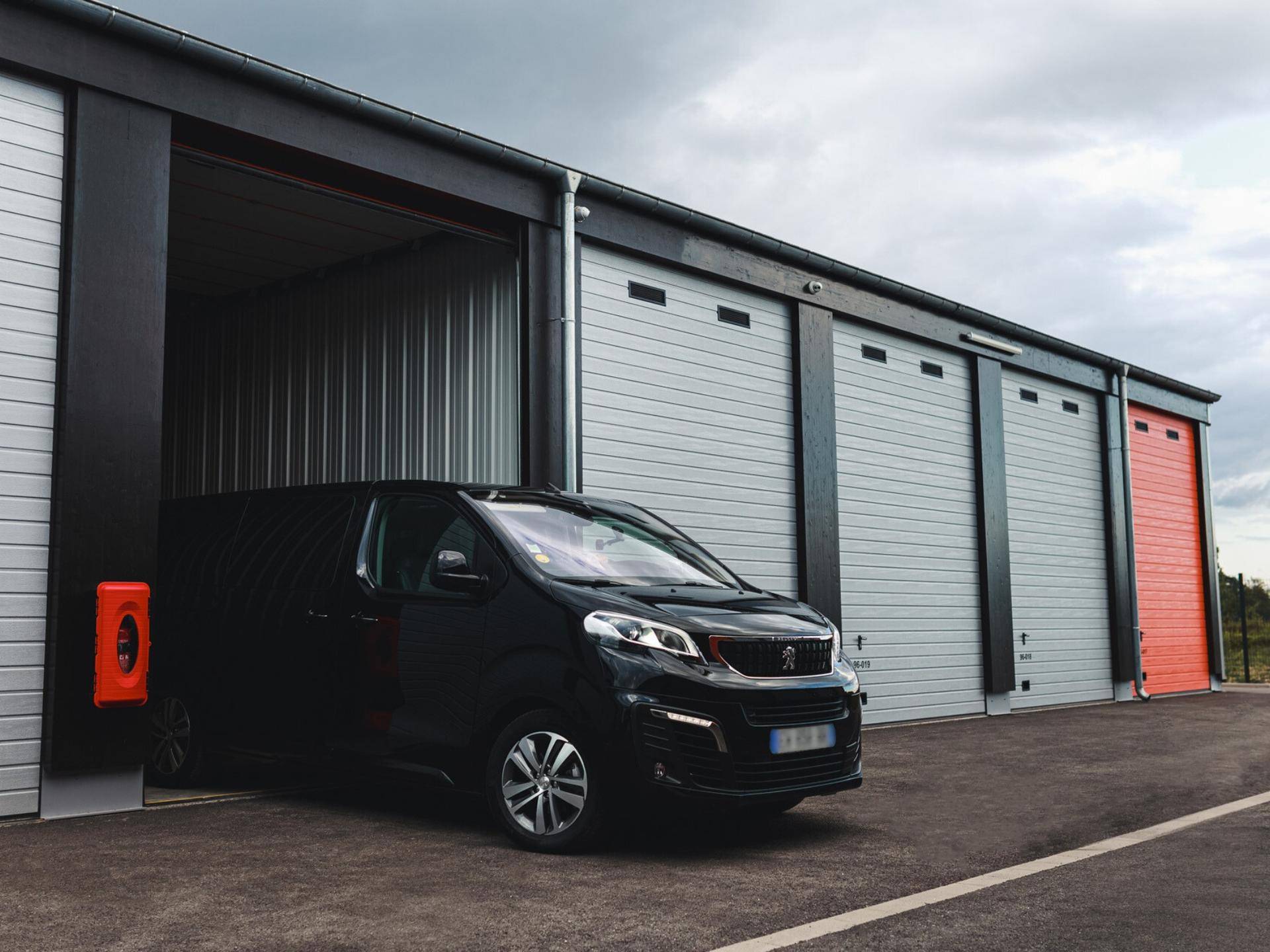Ein schwarzer Lieferwagen fährt in eine offene Lagerhalle, die als Garage dient.