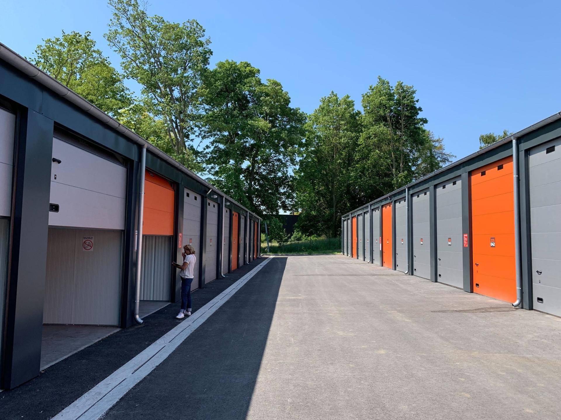 Zwei Reihen moderner Lagerhallen mit grauen und orangefarbenen Rolltoren unter einem klaren blauen Himmel.