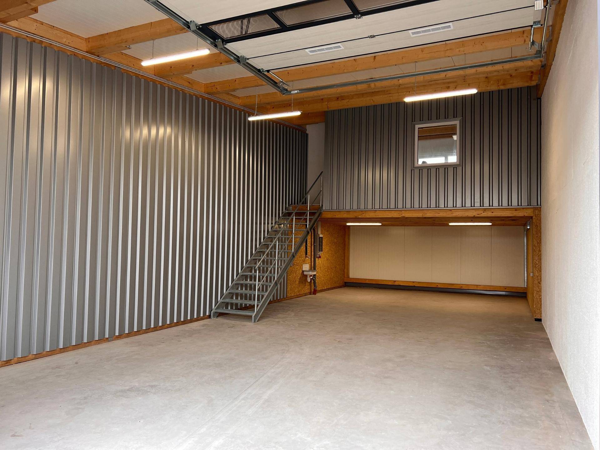 Industrielles Lager mit Wellblechwänden, Betonboden und einer Metalltreppe, die zu einer oberen Ebene führt.