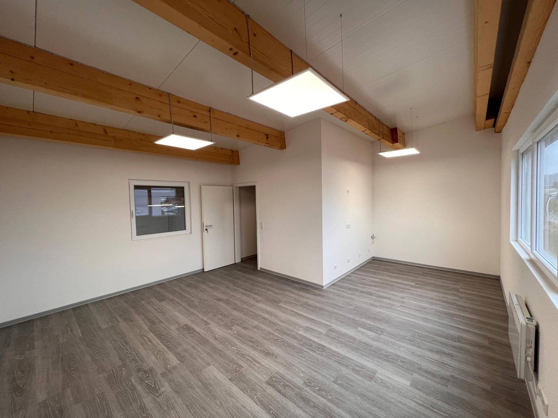 Helles Büro mit modernen LED-Leuchten, Holzbalkendecke und großen Fenstern, die viel Tageslicht hereinlassen.