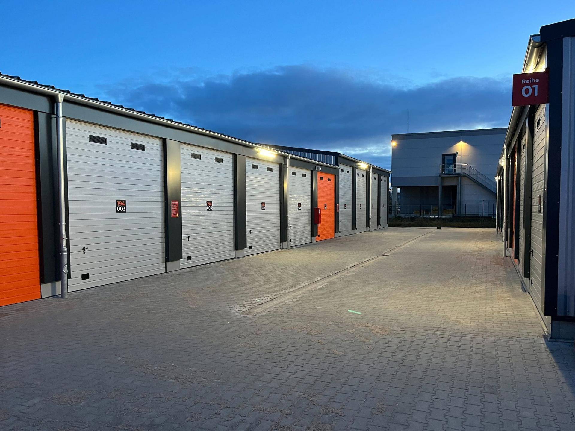 Reihen von Lagerhallen mit beleuchteten Eingängen in der Dämmerung, die eine moderne Anlage zeigen.