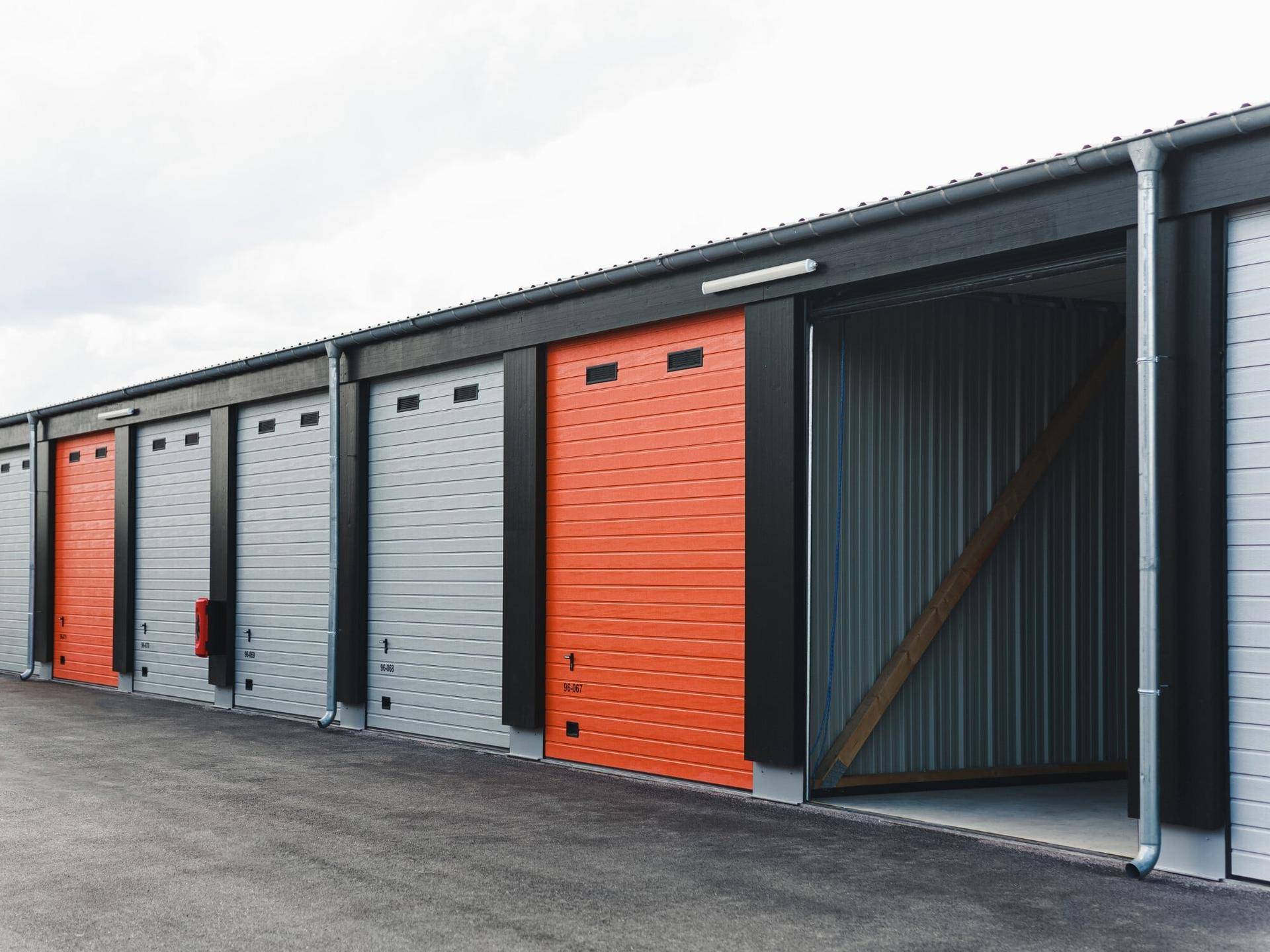 Reihe moderner Lagerhallen mit grauen und orangefarbenen Rolltoren, eine Einheit ist geöffnet.