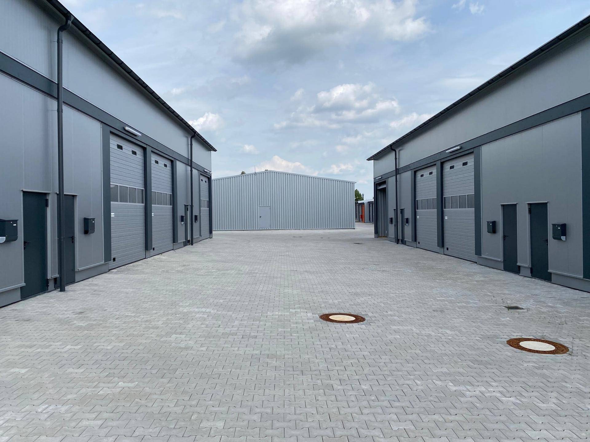 Außenansicht eines modernen Gewerbeparks mit mehreren Lagerhallen und gepflastertem Vorplatz.