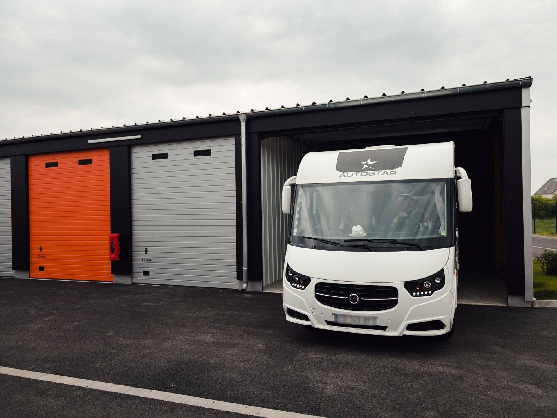 Weißer Campervan parkt vor einer offenen Lagerhalle mit Rolltor und moderner Architektur.