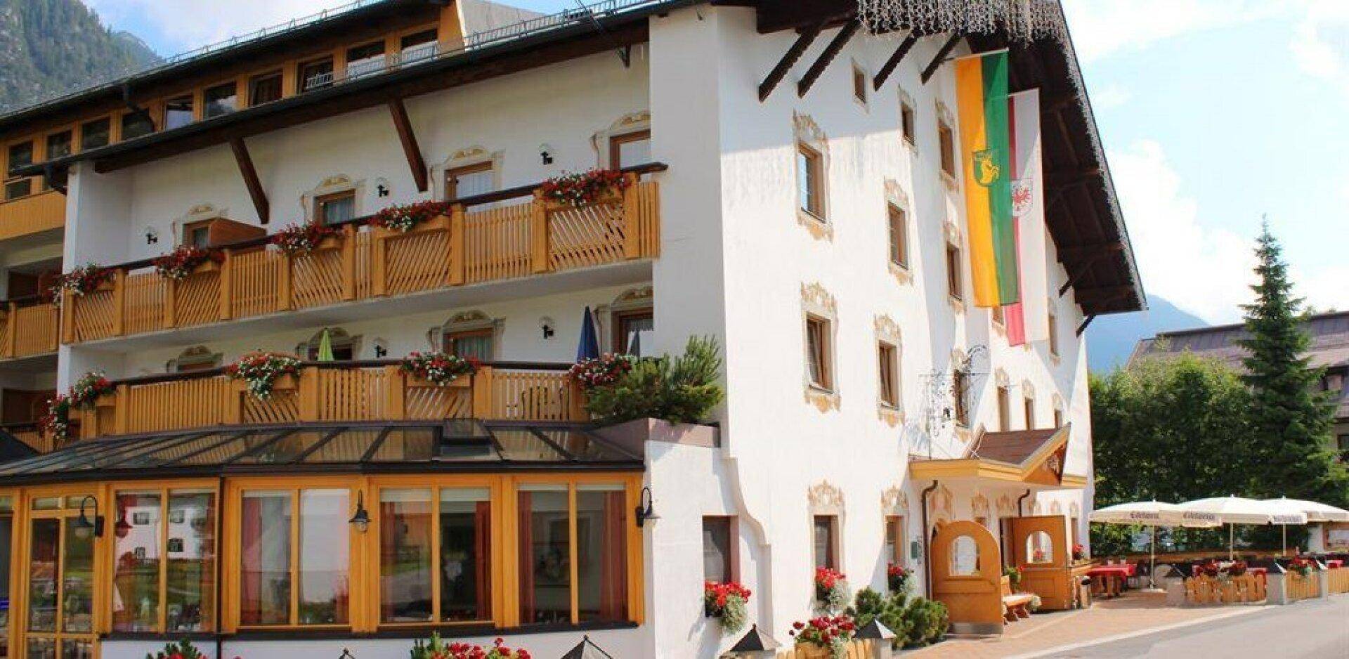 Detailansicht der Hotelaußenfassade im Sommer mit Holzbalkonen, Blumenkästen und einem verglasten Wintergartenbereich.