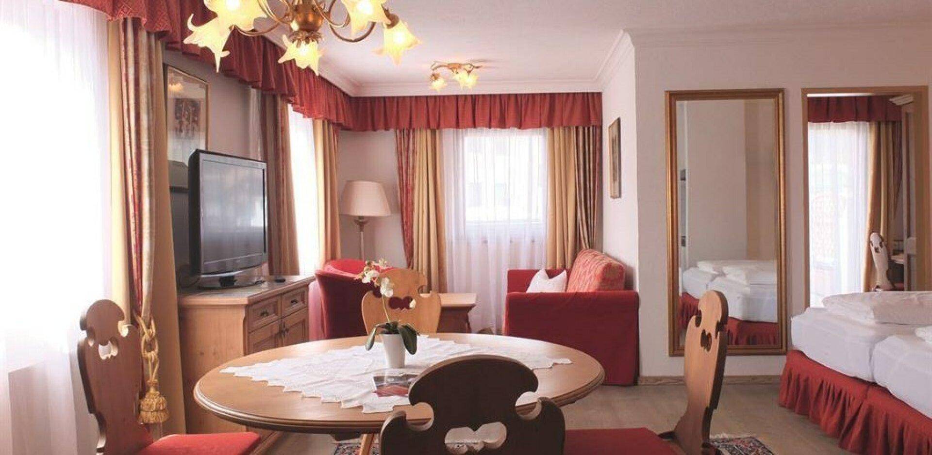 Komfortables Hotelzimmer mit einem Sitzbereich, einem Fernseher und traditioneller Einrichtung in warmen Rottönen.