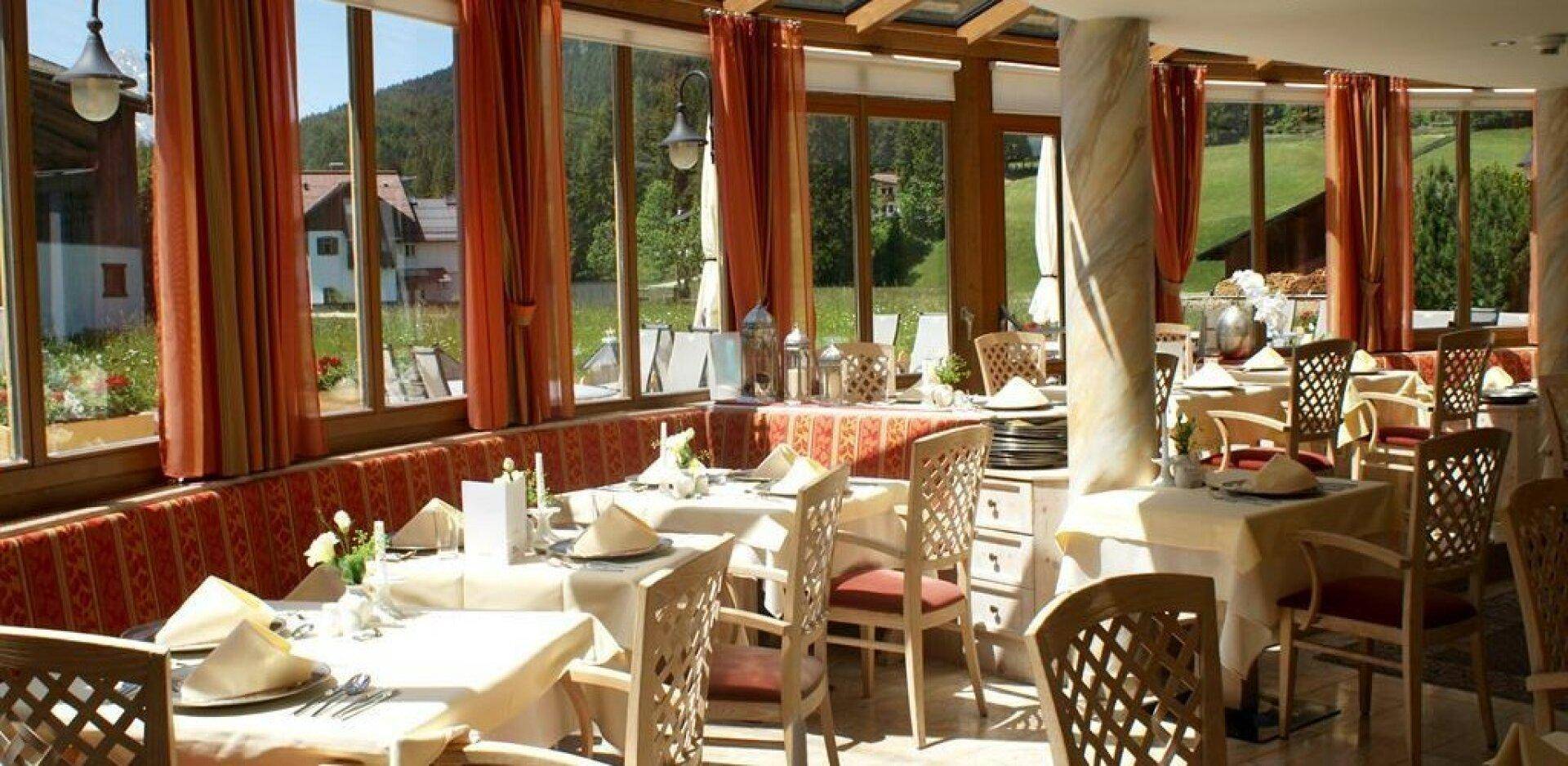 Heller Speisesaal mit großen Fenstern, die einen Blick auf die grüne Landschaft bieten, und elegant gedeckten Tischen.