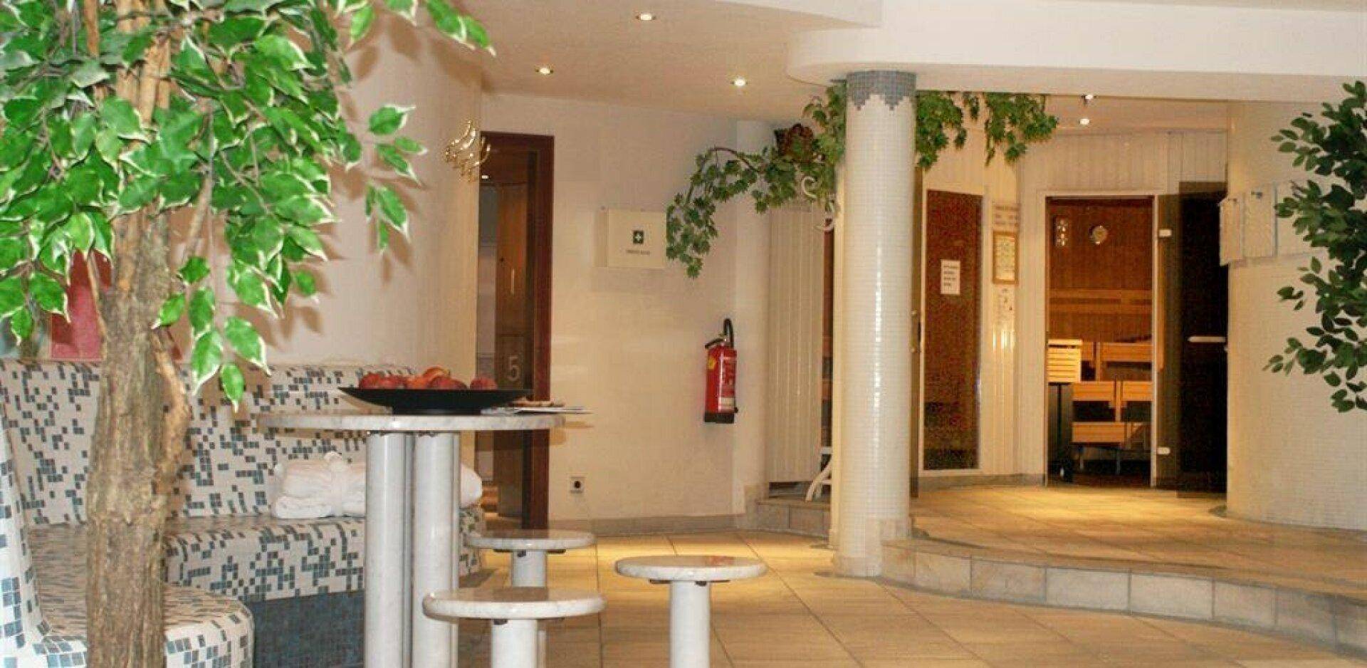 Entspannender Wellnessbereich mit Sitzgelegenheiten, Pflanzen und einem Eingang zu einer Sauna oder einem Dampfbad.