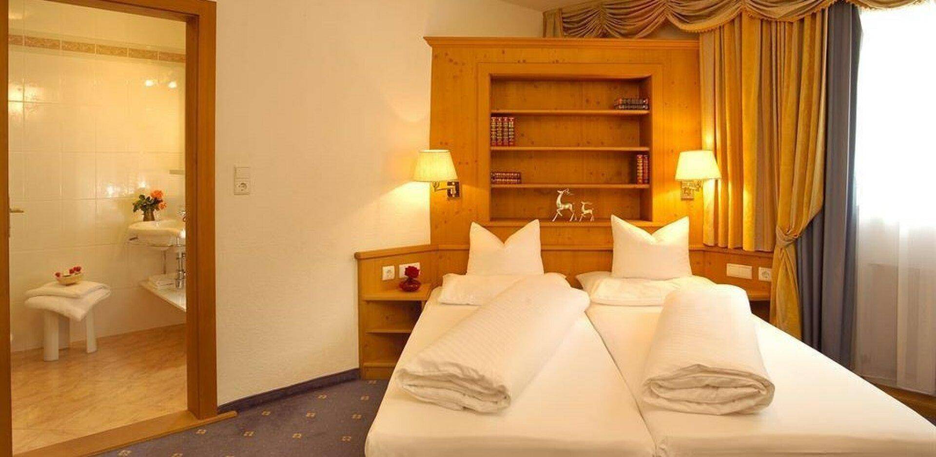 Gemütliches Schlafzimmer mit Holzmöbeln, Teppichboden und direktem Zugang zu einem gefliesten Badezimmer.