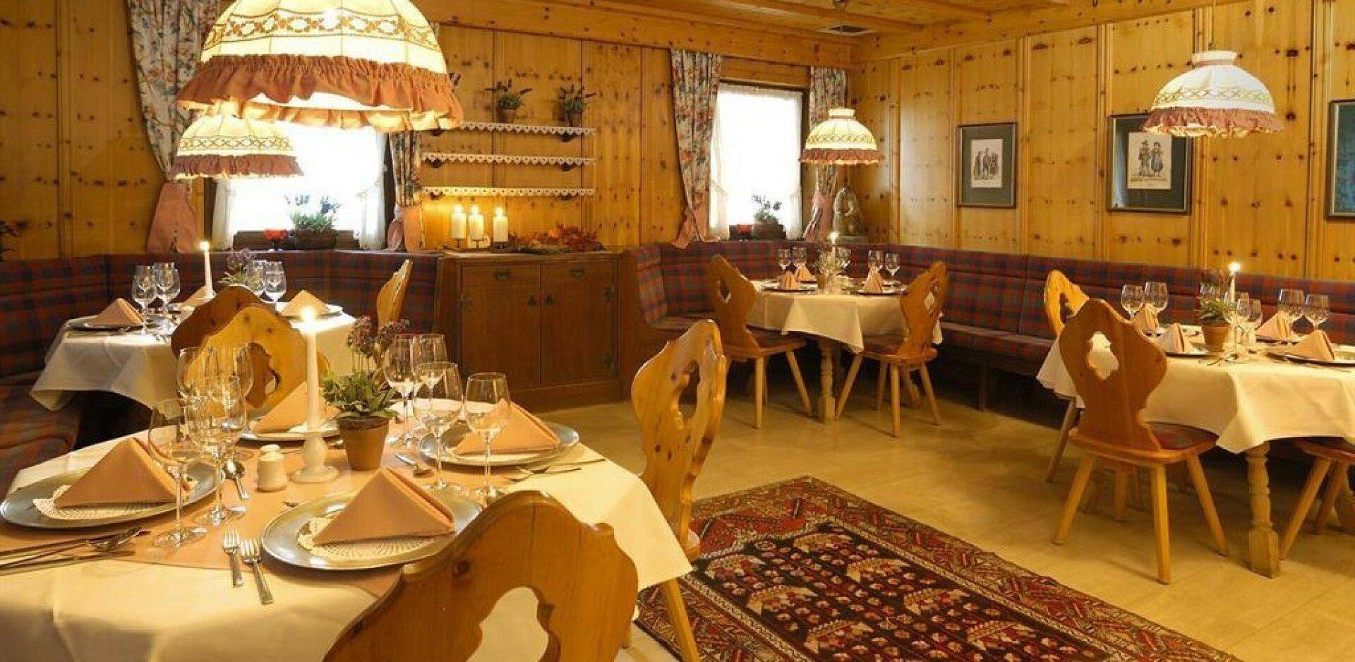 Gemütlicher Speisesaal im traditionellen Stil mit Holzwänden, gepolsterten Bänken und festlich gedeckten Tischen.