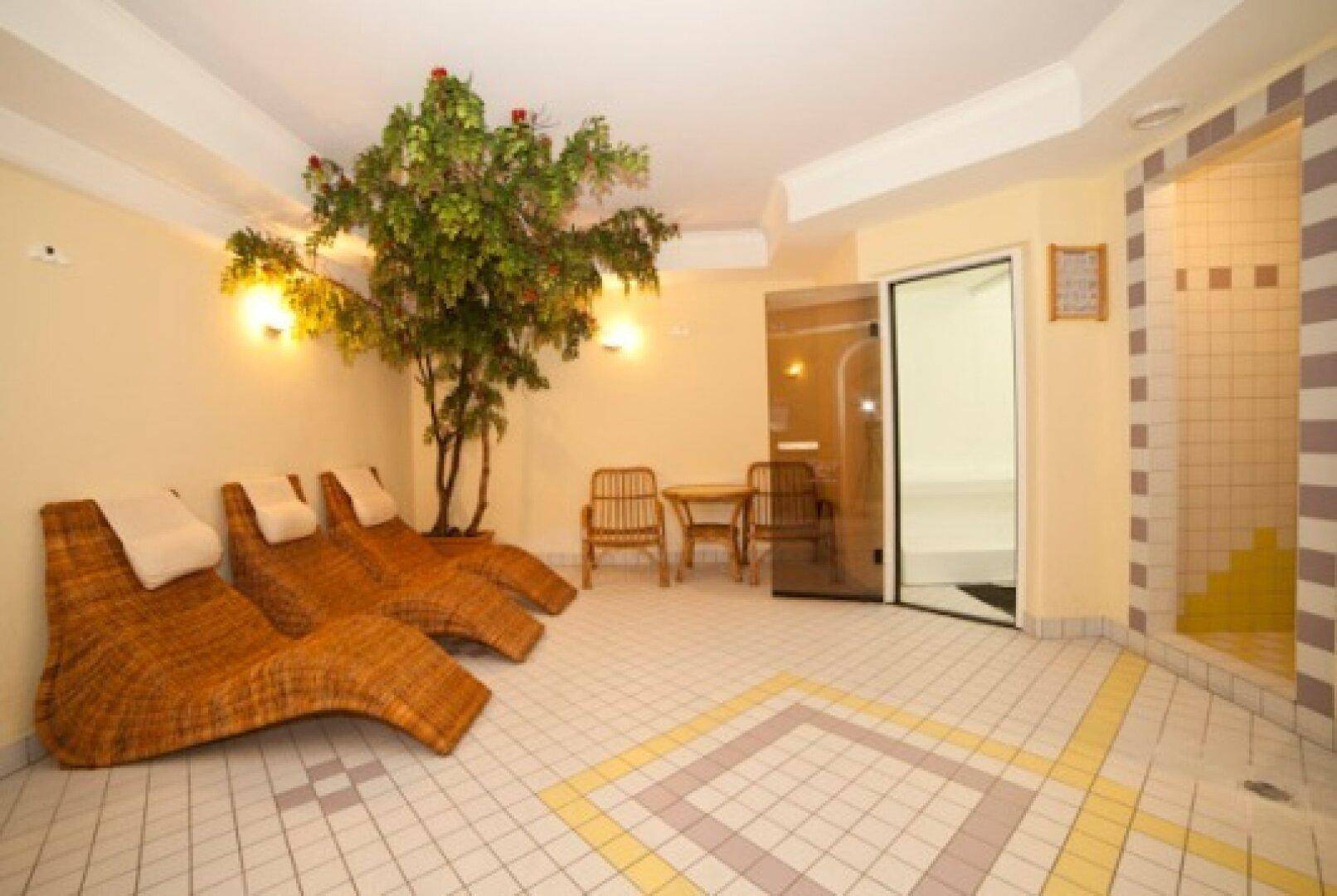 Wellnessbereich mit Liegen, Pflanzen und Zugang zur Sauna, hell und einladend gestaltet.