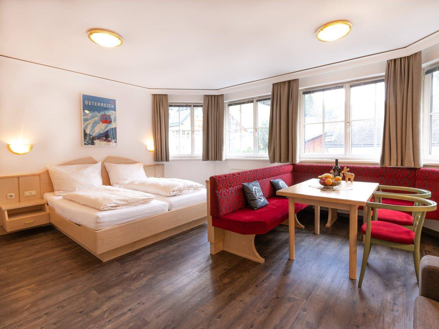 Gemütliches Studio-Apartment mit Schlafbereich, Essecke und Holzboden, hell durch große Fenster.