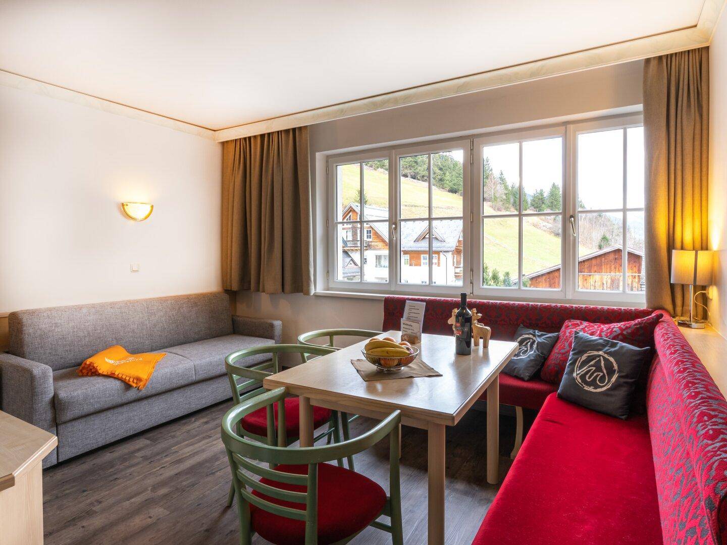Wohnbereich mit Essecke, Sofa und Blick auf die grüne Hügellandschaft durch große Fenster.