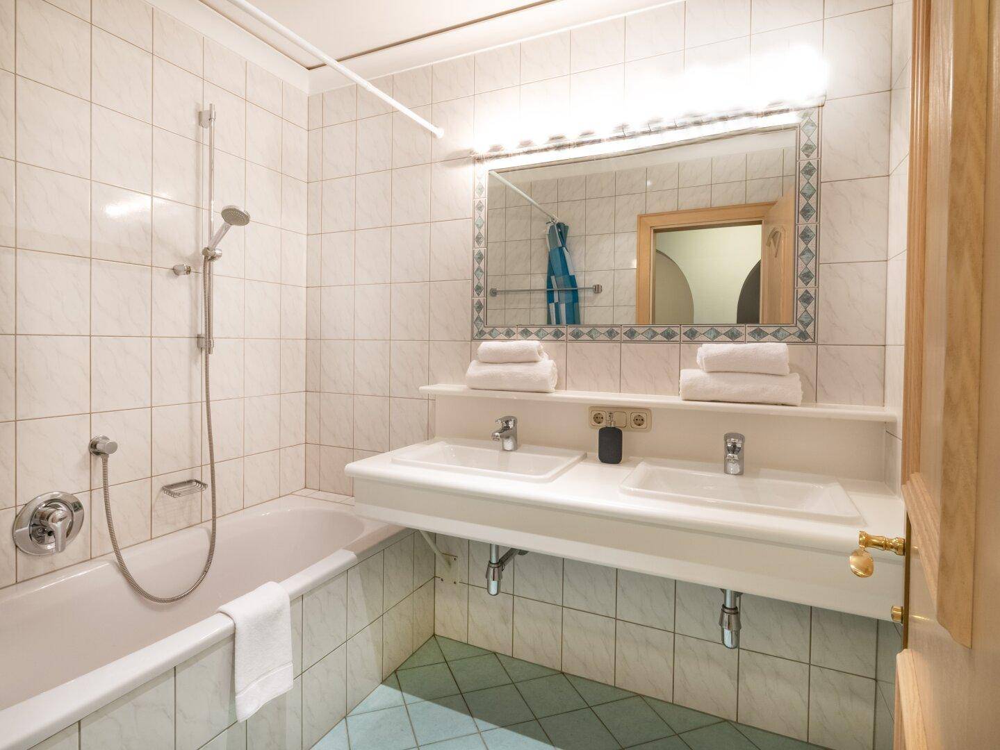 Helles Badezimmer mit Doppelwaschbecken, Badewanne und Duschvorrichtung, gefliest in Weiß und Blau.