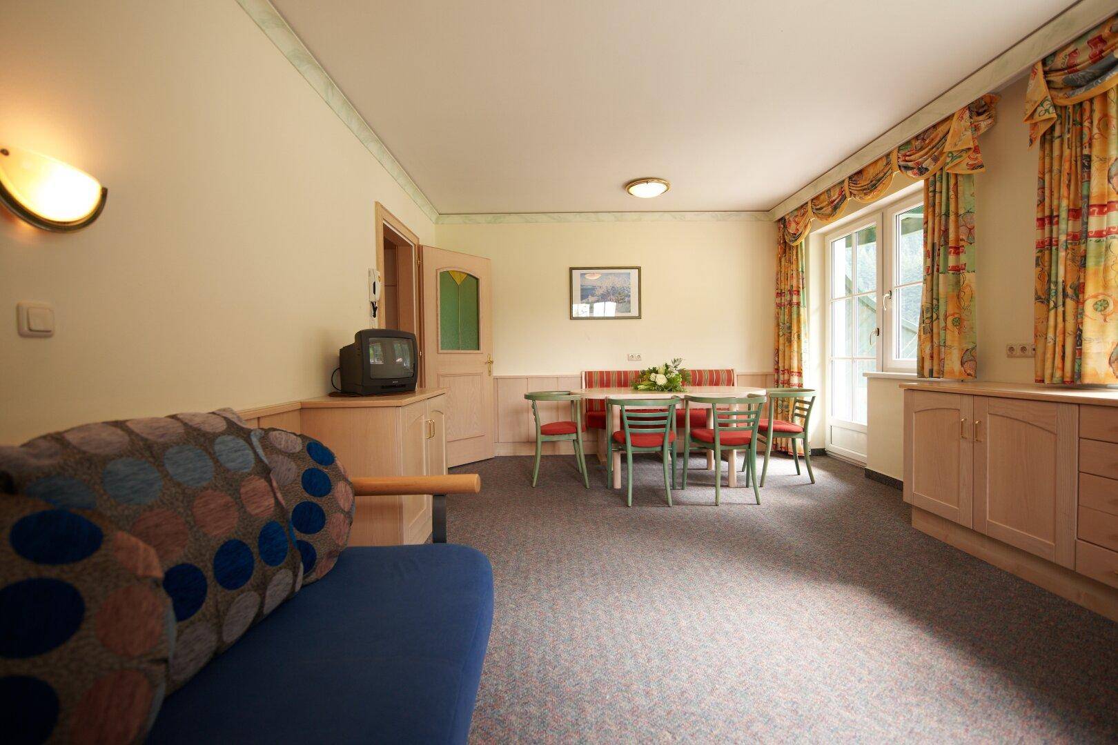 Geräumiger Wohn- und Essbereich mit Teppichboden, Esstisch und Sofa, hell durch Fenster.