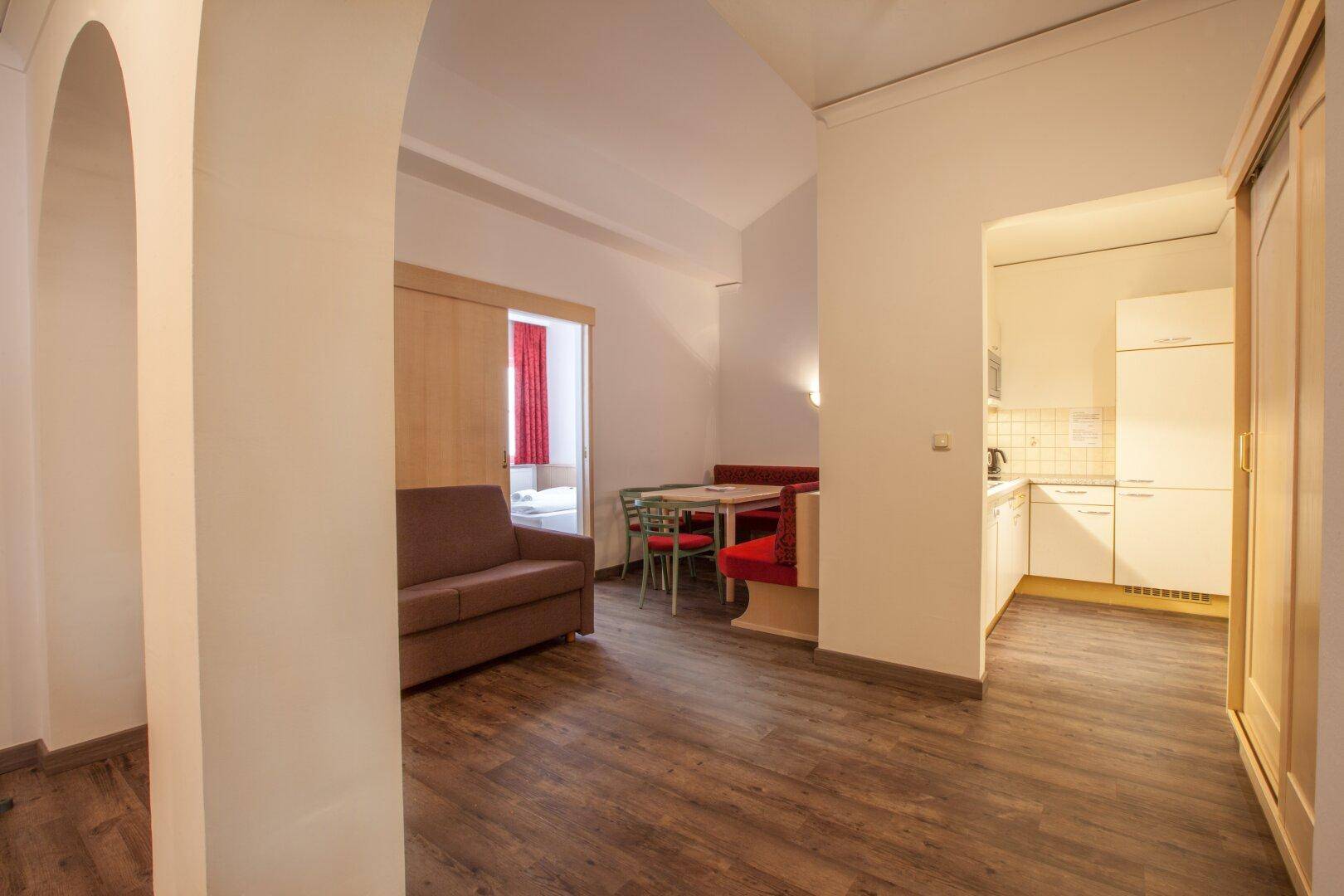 Offener Wohn- und Essbereich mit Holzboden und Zugang zu einem Schlafzimmer und einer Küche.