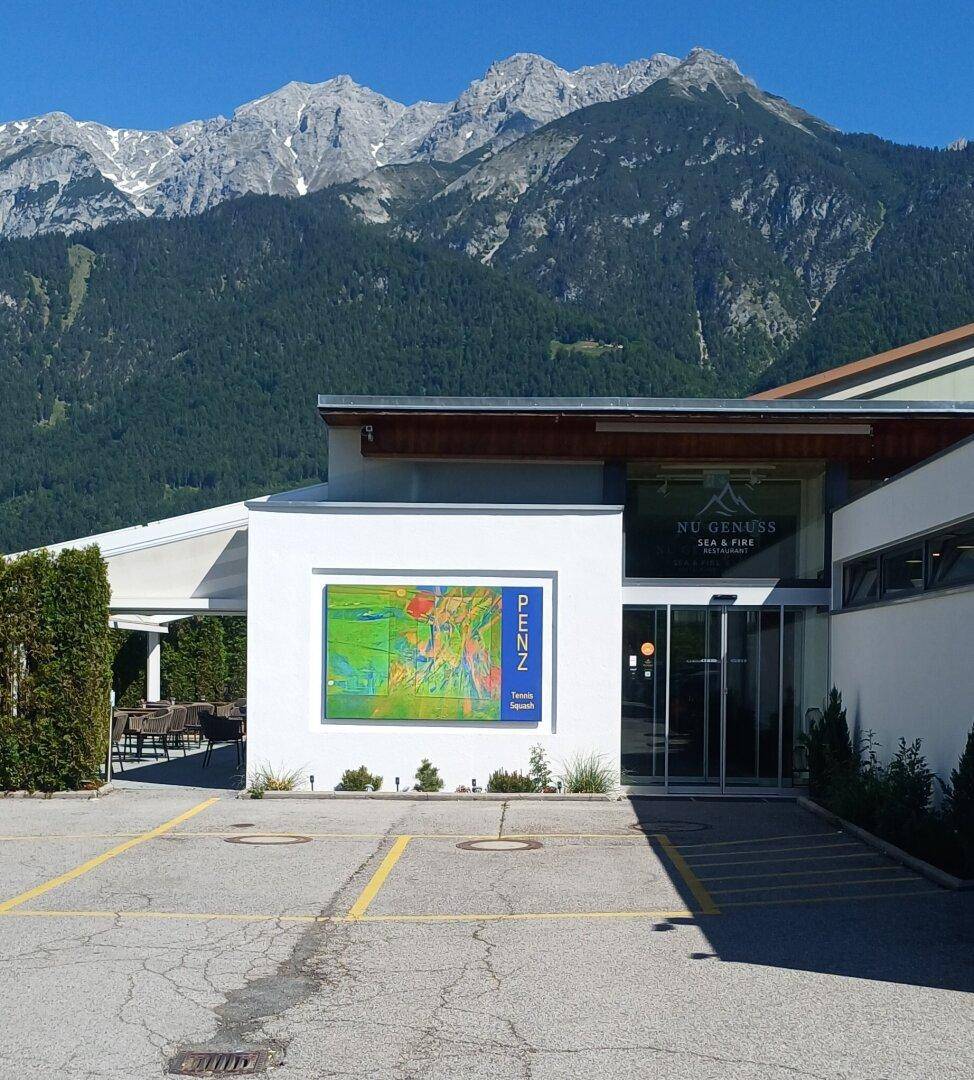 Modernes Gebäude mit Parkplätzen und beeindruckendem Bergblick im Hintergrund.