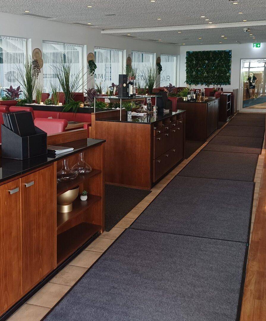 Innenansicht eines Restaurants mit Holzelementen, roten Sitzgelegenheiten und Teppichboden.
