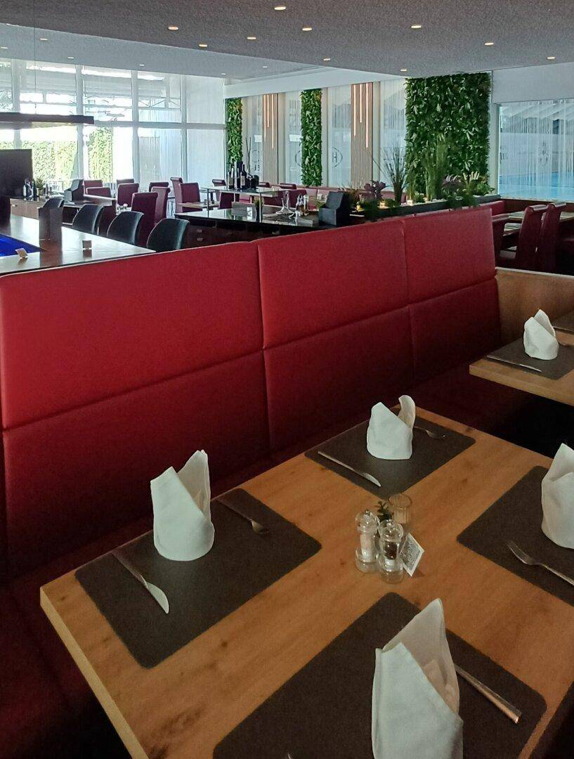 Gemütlicher Restaurantbereich mit roten Polsterbänken, Holztischen und gedeckten Plätzen.
