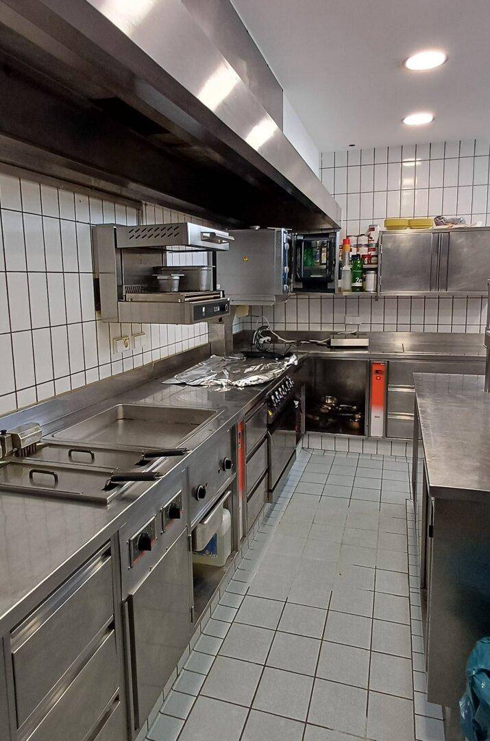 Professionelle Großküche mit Edelstahlgeräten, weißen Fliesen und Dunstabzugshaube.