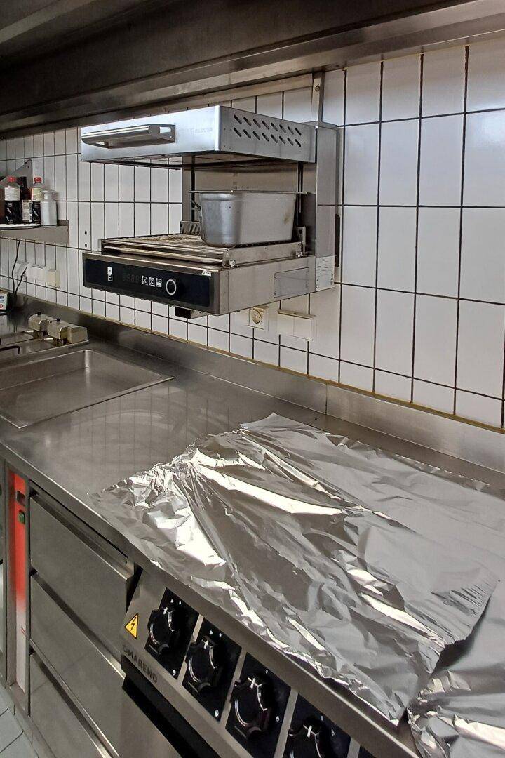 Professioneller Küchenbereich mit Edelstahlgeräten, Wärmelampe und weißen Fliesen.