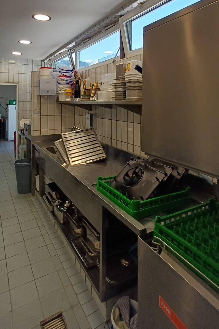 Spülbereich in einer Großküche mit Edelstahlspüle, Geschirrspüler und Ablageflächen.