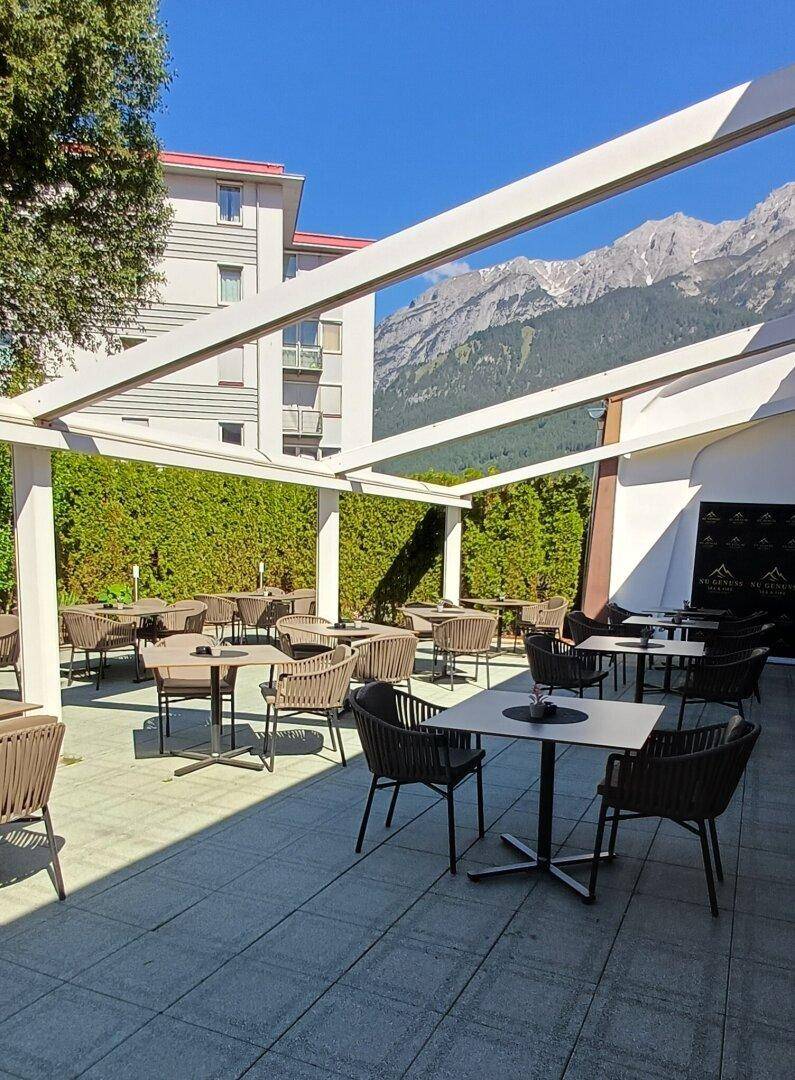 Große Außenterrasse mit Pergola, modernen Sitzgelegenheiten und Blick auf die Berge.