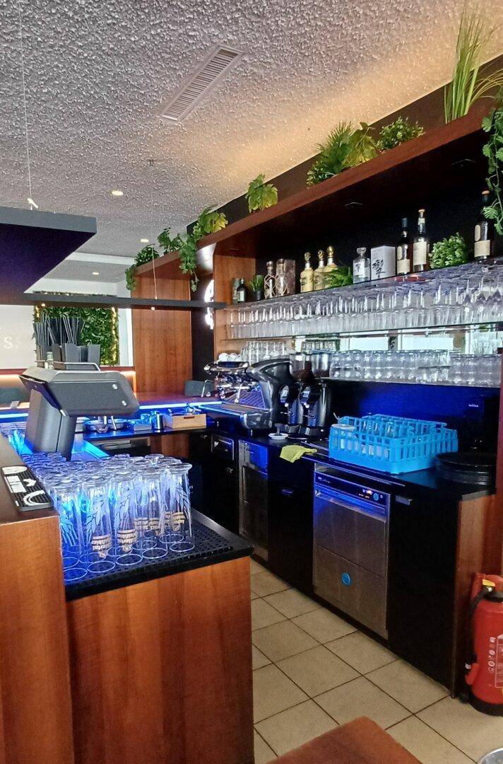 Moderne Bar mit blauer Beleuchtung, vielen Gläsern und einer Kaffeemaschine.