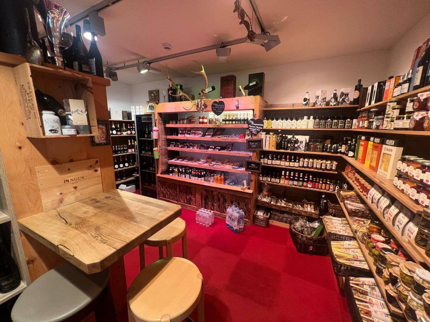 Gemütlicher Ladenbereich mit Holzregalen, einem kleinen Holztisch und Hockern auf leuchtend rotem Teppich.