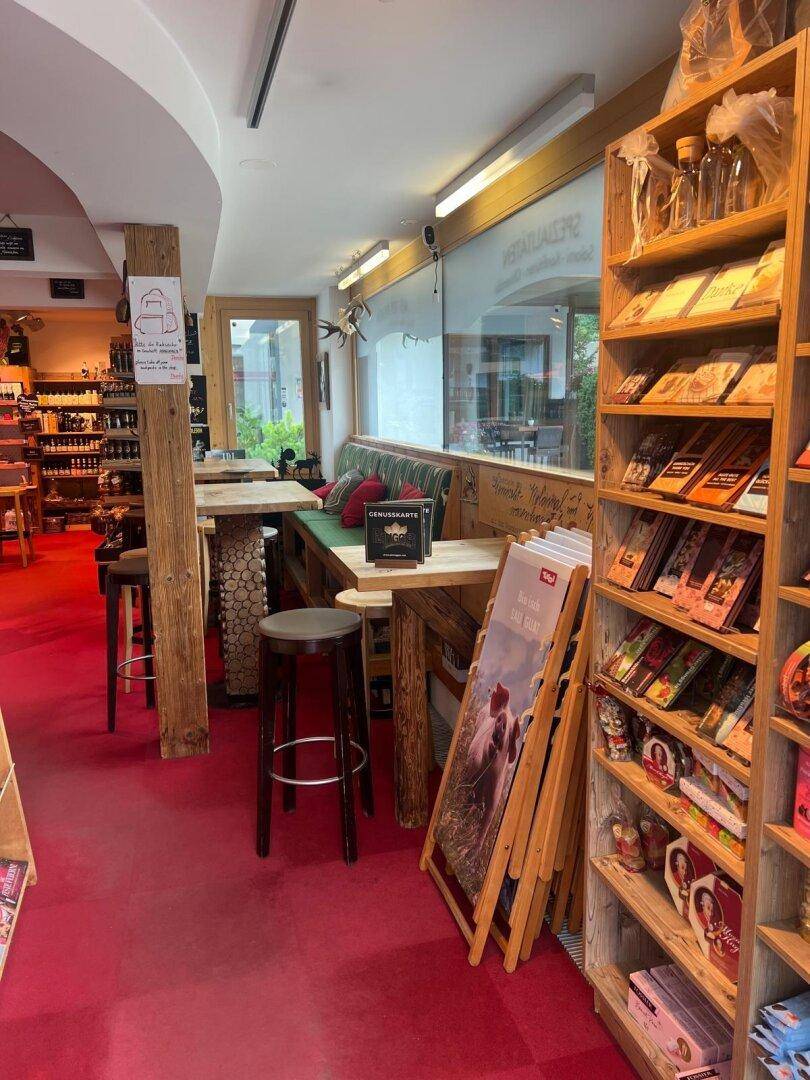 Sitzbereich in einem Bistro mit gepolsterter Bank, Holztischen und Hockern, neben einem Fenster.