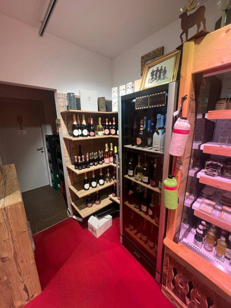 Weinabteilung in einem Geschäft mit Holzregalen und einem Weinkühlschrank, auf rotem Teppichboden.