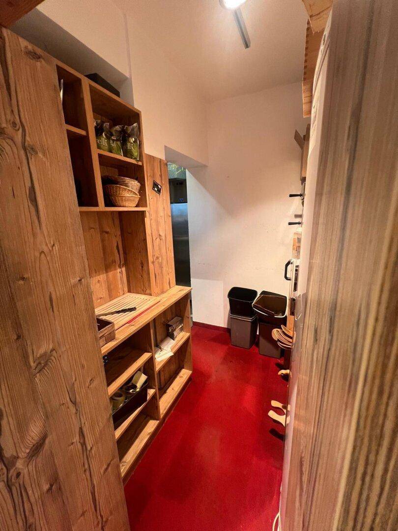 Hinterer Bereich eines Ladens mit Holzregalen und Abfalleimern, auf rotem Teppichboden.