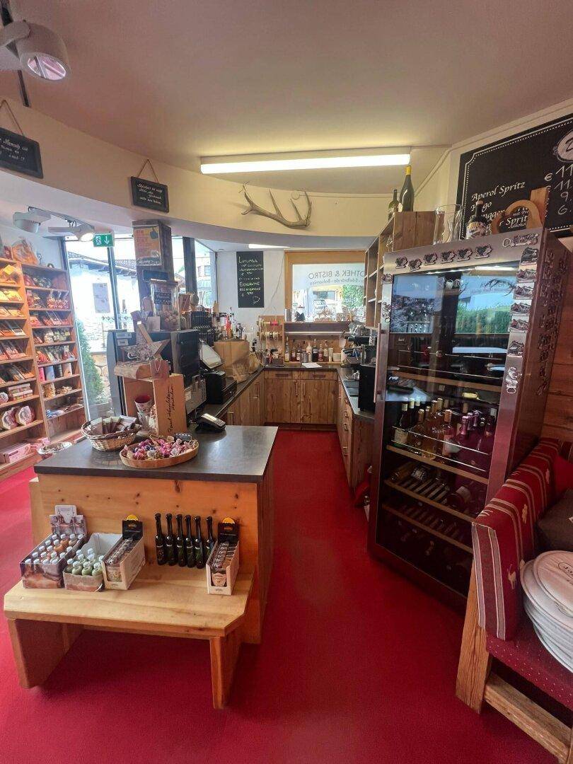 Thekenbereich in einem Bistro mit Kaffeemaschine, Auslagen und Holzmöbeln, auf rotem Teppichboden.