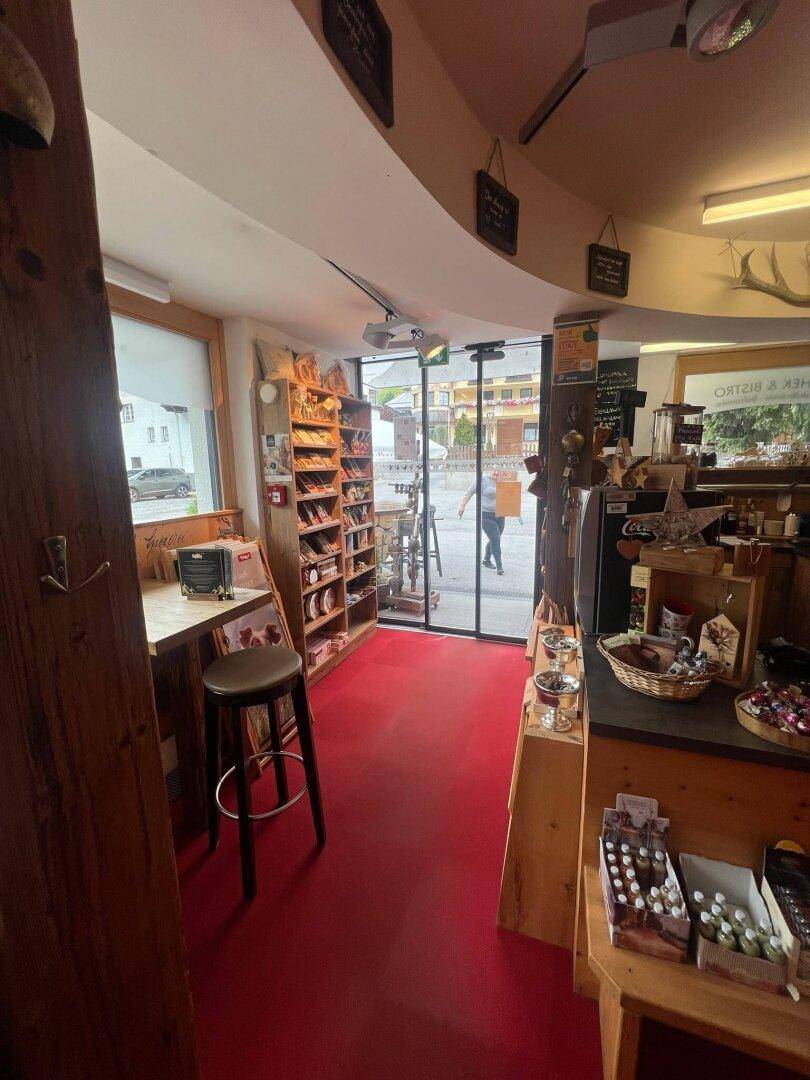 Blick durch einen Ladenbereich mit rotem Teppichboden und Holzregalen, die zur Eingangstür führen.