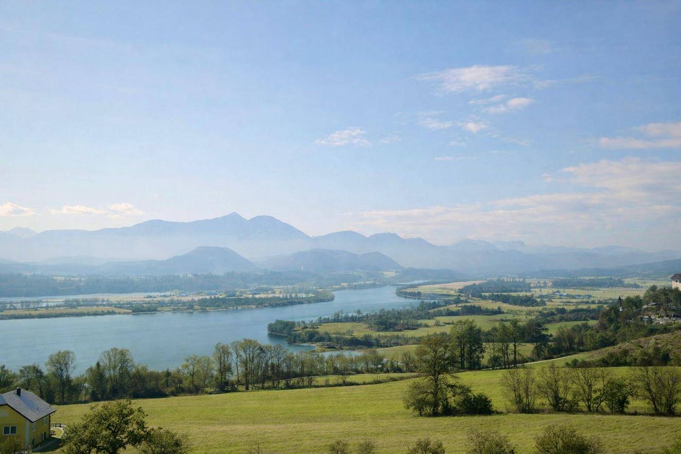 Panoramablick über eine weite Seenlandschaft mit grünen Hügeln und einer Bergkette am Horizont.