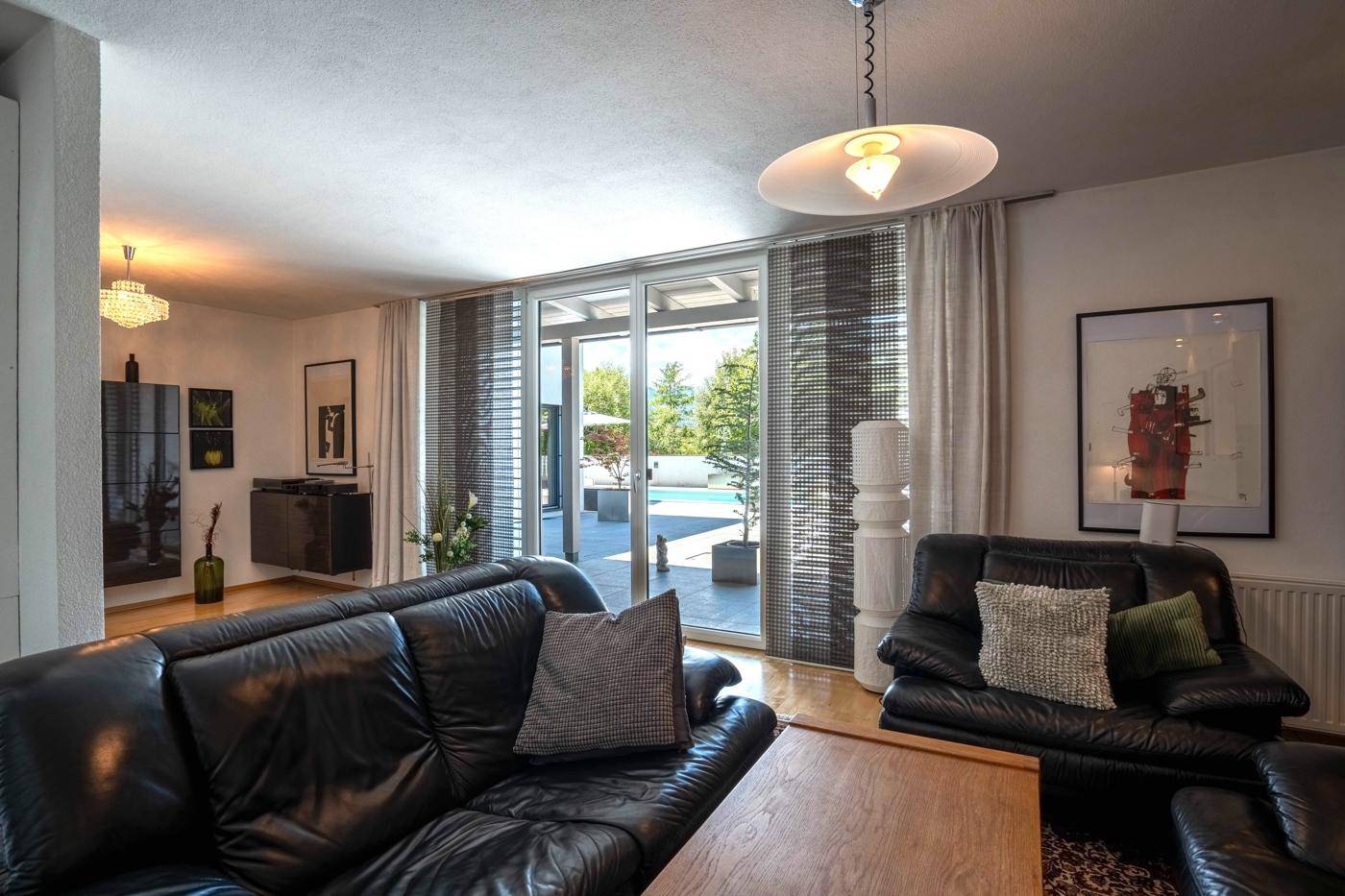 Gemütliches Wohnzimmer mit Ledersofas, Holzboden und Zugang zur Terrasse mit Poolblick.