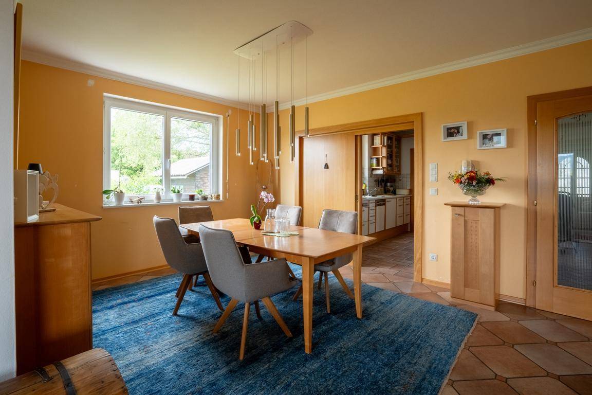 Heller Essbereich mit Holztisch, modernen Stühlen und Blick ins Grüne durch das Fenster.