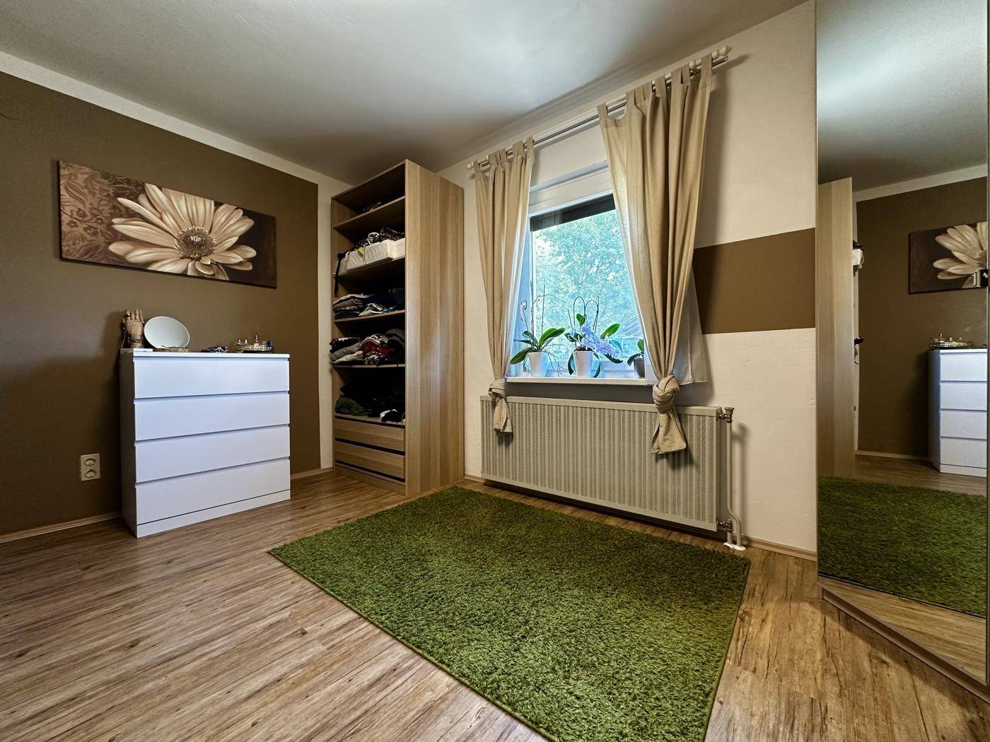 Schlafzimmer mit Holzboden, Kleiderschrank und Fenster, in warmen Brauntönen gestaltet.