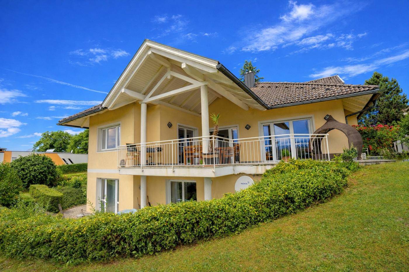 Rückansicht des Hauses mit großem überdachtem Balkon, Garten und weitem Blick in die Landschaft.