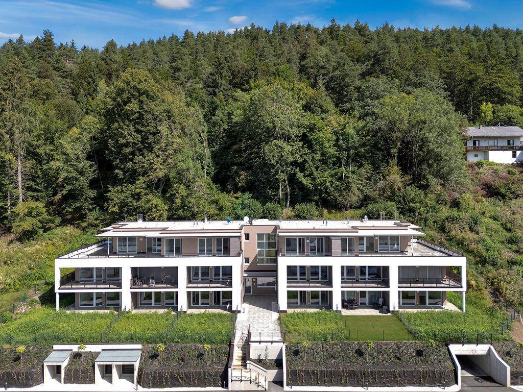 Gesamtansicht der modernen Wohnanlage am Hang, umgeben von üppiger Natur und mit Tiefgaragenzufahrt.