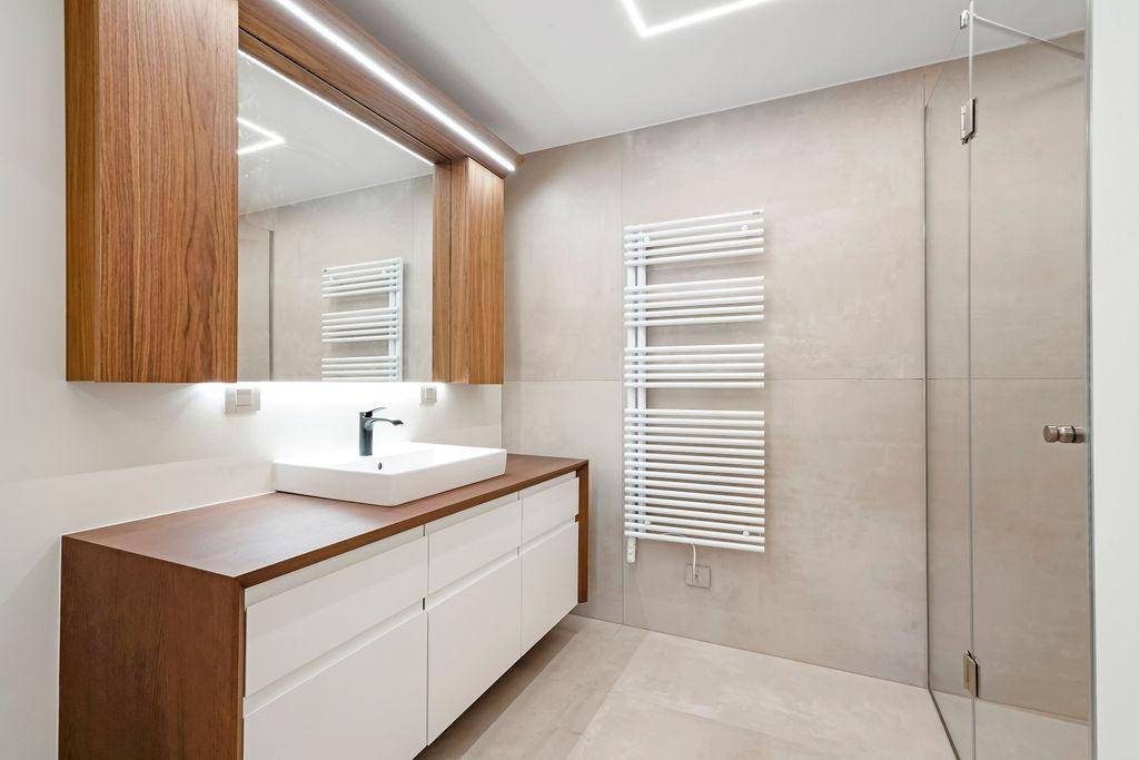 Modernes Badezimmer mit Holzwaschtisch, großem Spiegel, Handtuchheizkörper und begehbarer Dusche.