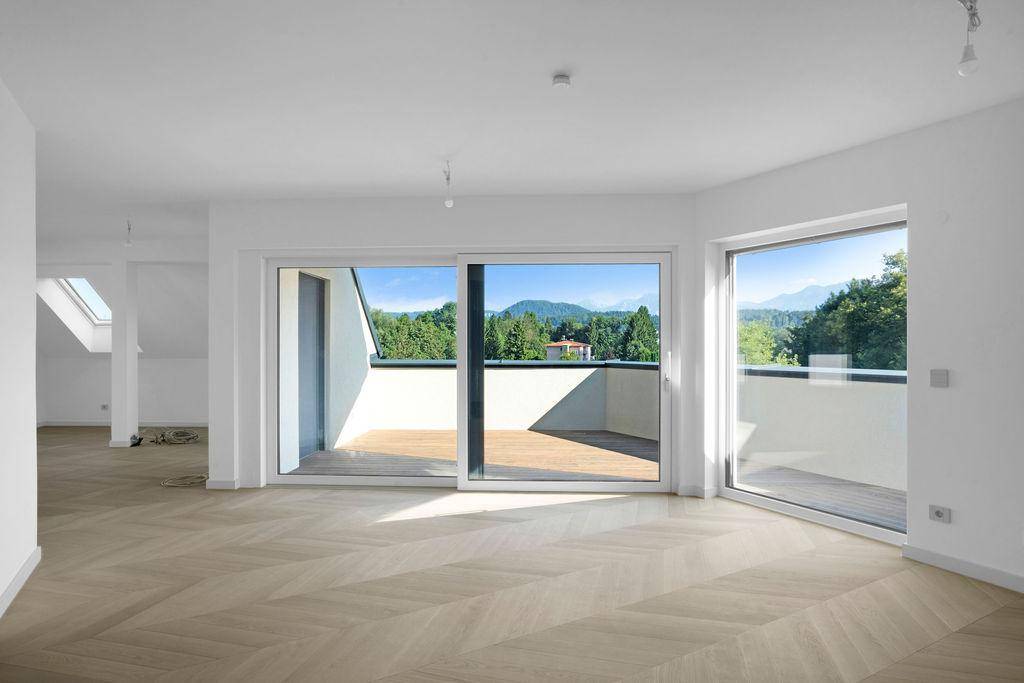 Heller Wohnraum mit Fischgrätparkett, großen Fenstern und Zugang zu einem Balkon mit Bergblick.