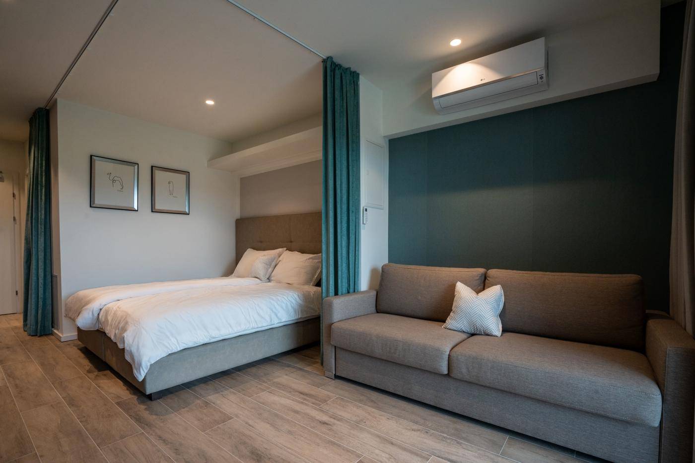 Modernes Schlafzimmer mit Doppelbett, Sofa und Klimaanlage, durch Vorhang abgetrennt.
