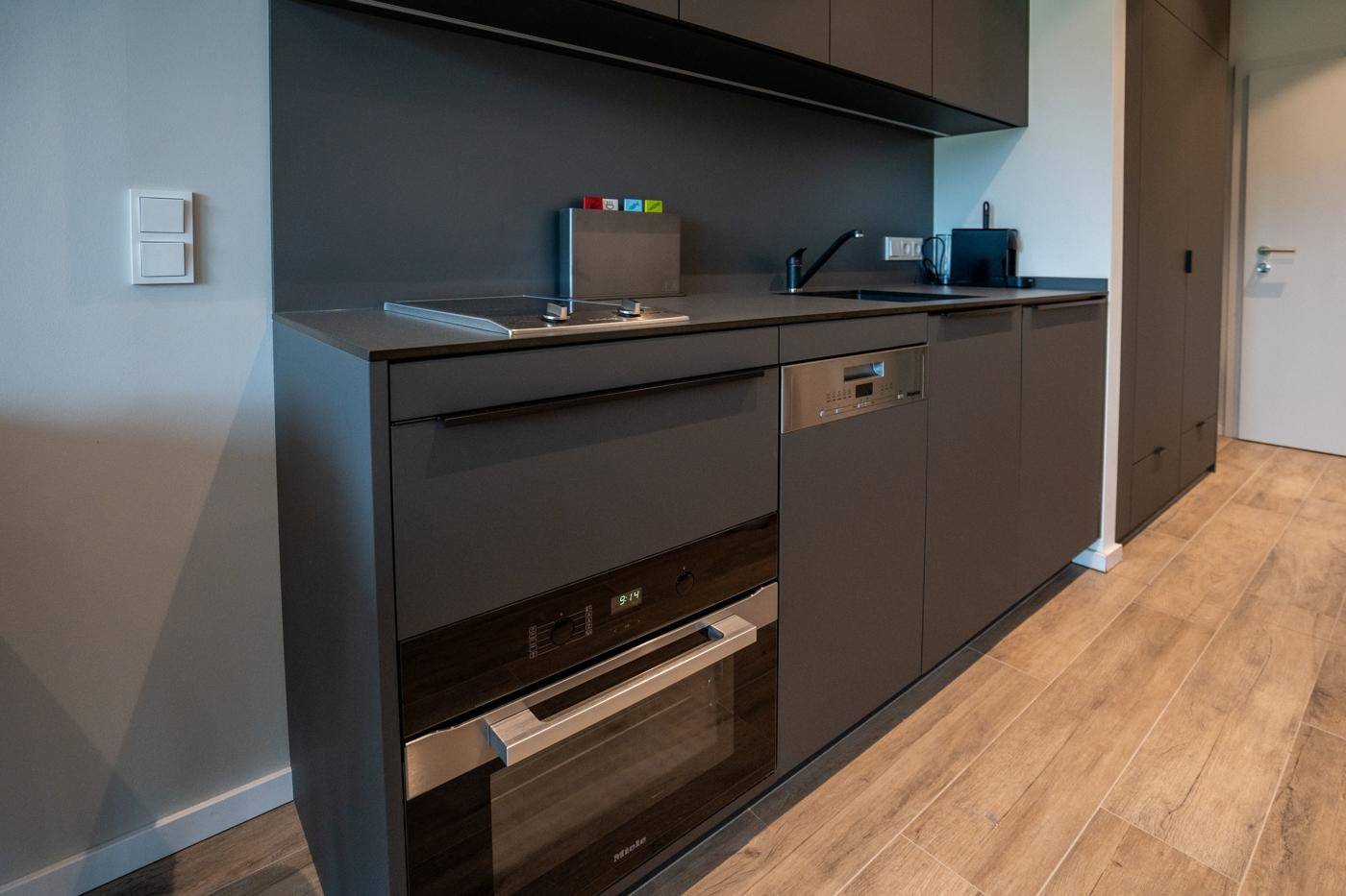 Moderne Küchenzeile in Dunkelgrau mit integriertem Backofen und Geschirrspüler.
