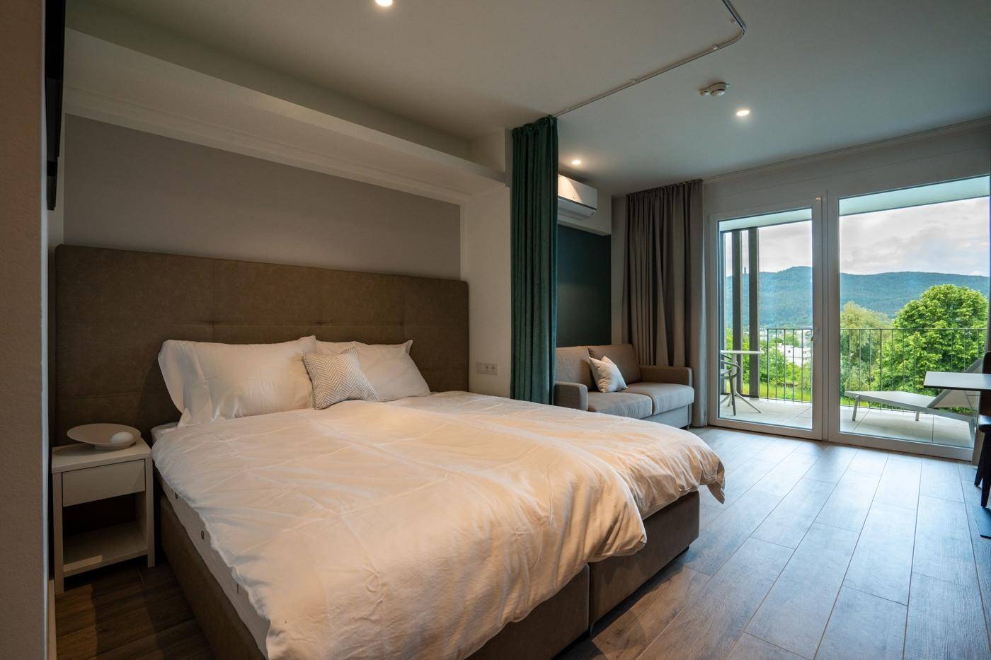 Helles Schlafzimmer mit Doppelbett, Balkonzugang und Blick auf die grüne Landschaft.