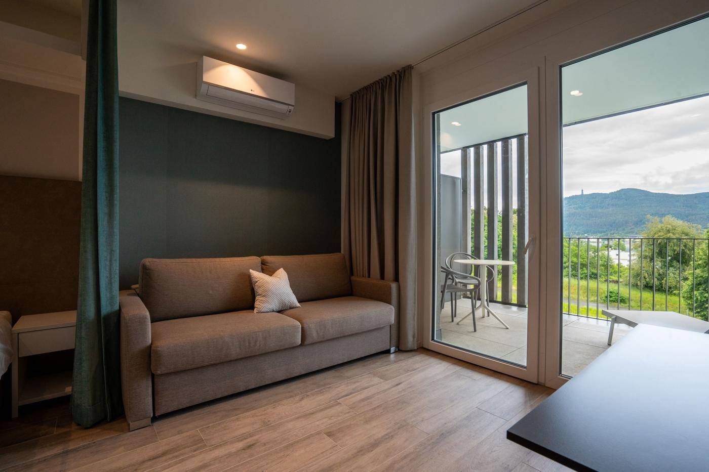 Wohnbereich mit bequemem Sofa, Klimaanlage und großen Fenstern zum Balkon mit Aussicht.