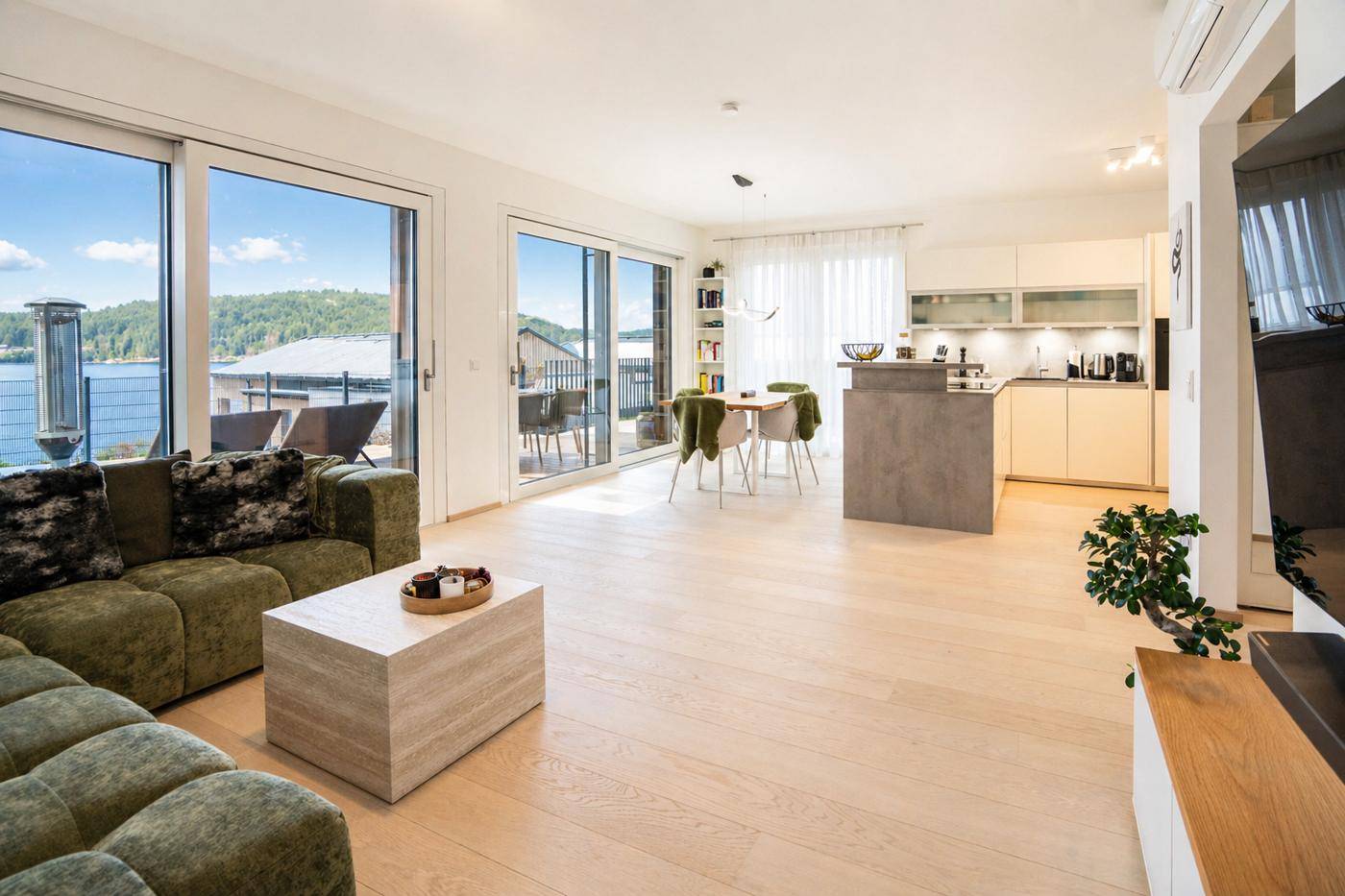 Heller offener Wohn-Essbereich mit moderner Küche und großen Schiebetüren zum Balkon mit Seeblick.