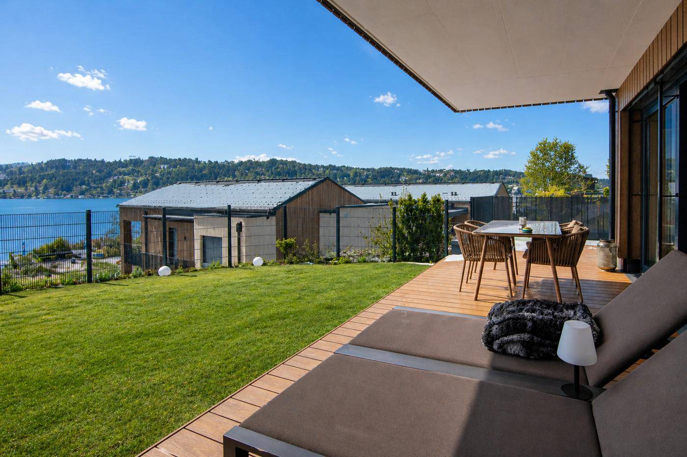 Große Terrasse mit Holzdeck, Rasenfläche und Liegestühlen mit Panoramablick auf den See.