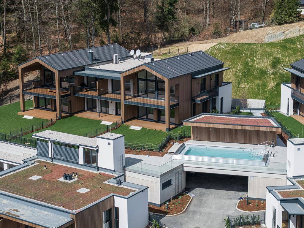 Luftaufnahme einer modernen Wohnanlage mit Holzhäusern, Gründächern und einem eleganten Poolbereich.
