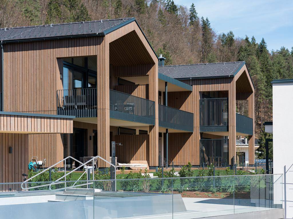 Moderne Wohngebäude mit Holzfassaden und Balkonen, umgeben von Grünflächen und einem Poolbereich.